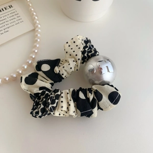 Détail d'un chouchou à pois noirs et blancs avec un pendentif sphérique argenté lettre H