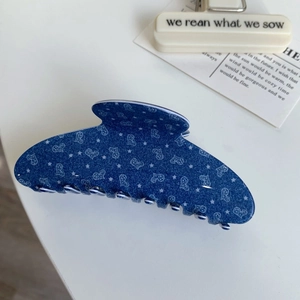 Close-up of a blue acetate hair claw clip with star and heart patterns and denim texture