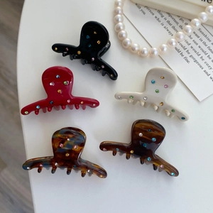 Set dettagliato di cinque mollette in acetato con strass colorati su sfondo di perle