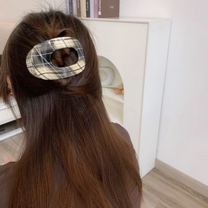 Close-up of a checkered pattern oval hair clip worn on a woman's long brown hair