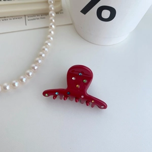 Dettaglio della molletta per capelli in acetato bordeaux con strass colorati su fondo bianco