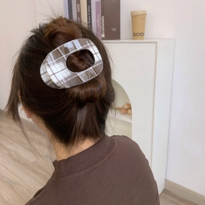 Detailed back view of a woman wearing a large brown plaid hair claw clip in a stylish bun
