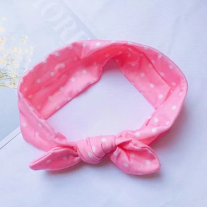 Vue détaillée d'un bandeau bébé en coton rose à pois avec un élégant nœud torsadé