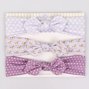 Detailed view of three purple baby bow headbands on a decorative display card