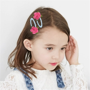 Dettaglio di fermagli per capelli con rose in tessuto rosa e foglie su clip BB blu