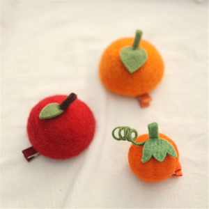 Detailed close-up of handmade wool felt apple and orange hair clips on fabric