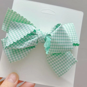 Détail d'une pince à cheveux nœud en tissu à carreaux vert et blanc avec bords dentelés