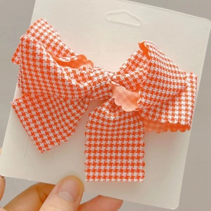 Détail de la pince à cheveux en tissu à carreaux orange et blanc avec bords dentelés
