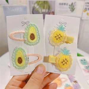 Close-up of embroidered avocado and pineapple hair clips for kids on a card