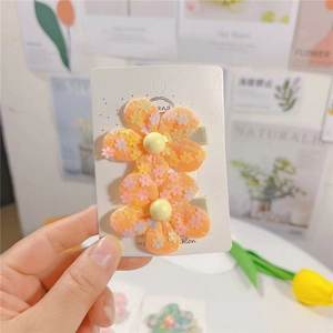 Gros plan de barrettes fleurs en maille orange avec paillettes et perle centrale