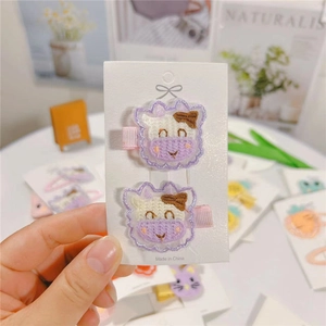 Detail of embroidered cartoon cow hair clips with purple fabric wrapped safety pins