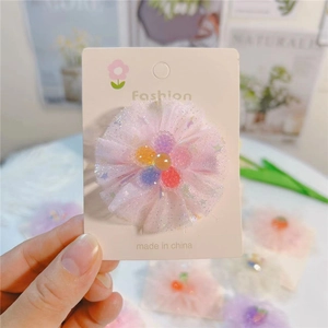 Détail d'une pince à cheveux en tulle rose avec perles sur une carte de présentation