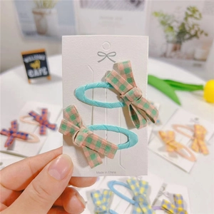 Close-up of a pair of blue plaid bow hair clips on a white card display for girls