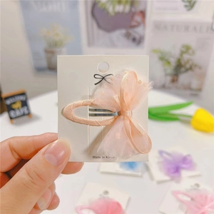 Close-up of pink polka dot mesh bow hair clip on white card board held by hand