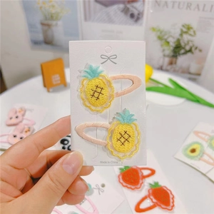 Detail view of two embroidered pineapple hair clips for toddlers on a white display card