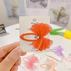 Close-up of vibrant orange mesh bow hair clip on a display card for children
