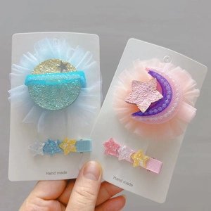 Détail de deux pinces à cheveux étoile et lune avec paillettes et ruban en maille