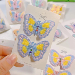 Close-up of embroidered butterfly hair clips with colorful rhinestones on a card