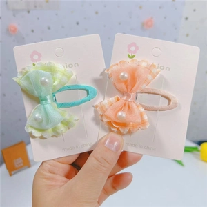 Détail de nœuds à carreaux verts et orange avec tulle et perles sur barrettes à cheveux