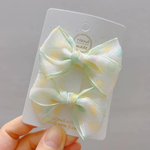 Detailed view of handmade polka dot bow hair clips in light green and yellow organza