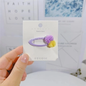 Dettaglio del fermaglio per capelli BB in nastro viola con graziosi pompon gialli e viola