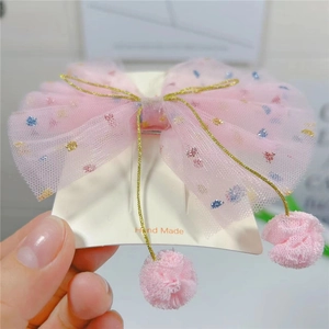 Détail d'une pince à cheveux avec nœud en tulle rose scintillant et pompons suspendus