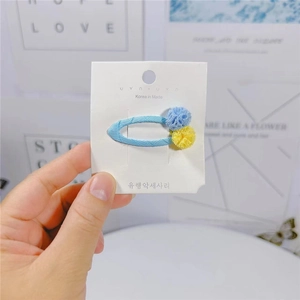 Dettaglio della molletta per capelli colori caramella con pompon blu e gialli su carta