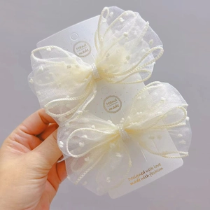 Detail view of two off-white polka dot sheer tulle bow hair clips on display card