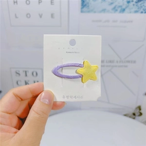 Dettaglio di un fermaglio per capelli in tessuto viola con stella gialla glitterata su carta