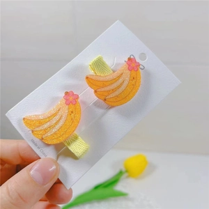 Close-up of glittery yellow banana hair clips for girls on a white card display