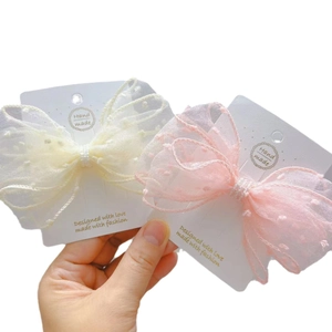 Pink and beige polka dot mesh bow hair clips with pearls on a display card