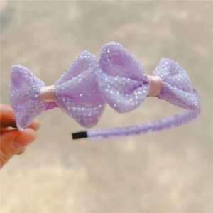 Detail showing hand holding double sequined bow headband for girls in light purple