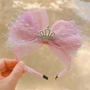 Detailed view of a pink tulle bow headband with a silver crown emblem for girls