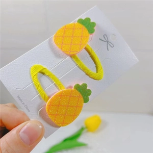 Detail of yellow pineapple hair clips with glitter finish and green felt leaves on white card