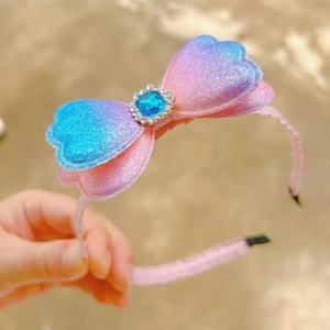 Détail d'un serre-tête en dentelle rose avec nœud pailleté dégradé et pierre bleue