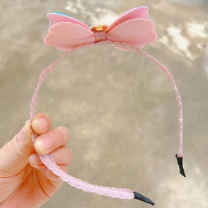 Gros plan détaillé d'un serre-tête en satin rose avec nœud et accent floral doré