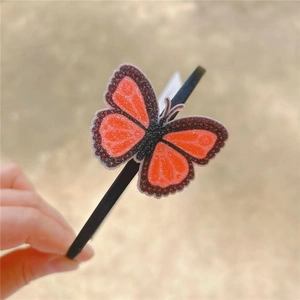 Detailed view of the sparkling glitter orange butterfly on a black girl headband