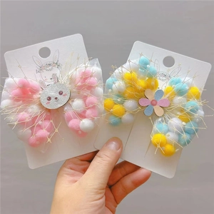 Detail of cute bow hair clips with rabbit charms and colorful pom-poms on display card
