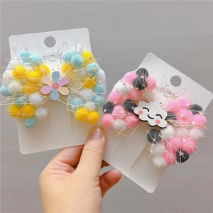 Detailed view of kids' hair clips with mesh-covered pom poms, flowers, and smile clouds