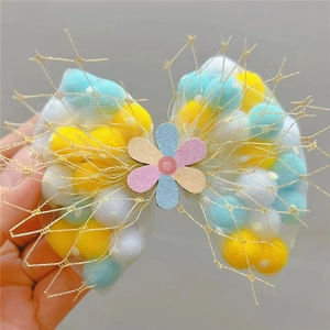 Detail of glitter mesh bow hair clip with colorful pom-poms and small flower center