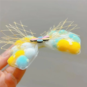 Close-up of children's mesh bow hair clip with colorful pom-poms and resin flower detail