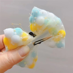 Close-up of mesh bow hair clip with colorful pompom fillings and metal alligator clip