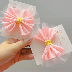 Détail de barrettes à carreaux roses avec centre jaune et tulle blanc sur carte papier