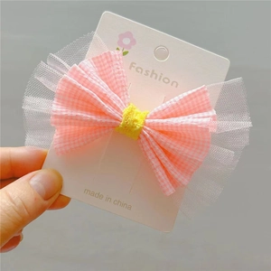 Détail de la barrette à nœud rose à carreaux avec bordure en dentelle et centre jaune