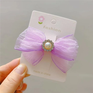Detail of a purple mesh bow hair clip with a pearl rhinestone center on a white card