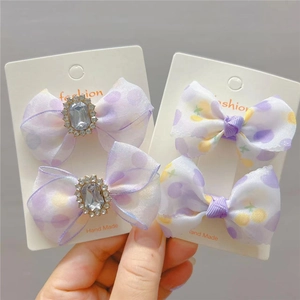 Détail de quatre pinces à cheveux nśuds avec pois violets et pierres sur emballage