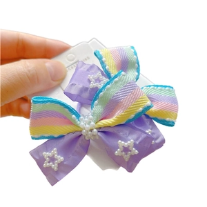 Hand holding a colorful striped bow hair clip with pearl stars for kids' hairstyles