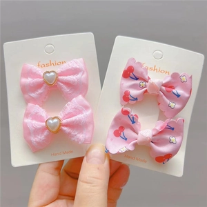Détail de barrettes à nœuds roses en dentelle et motifs cerises avec perles factices