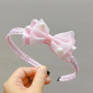 Dettaglio fascia rosa per bambine con fiocco in tulle e perline bianche su sfondo grigio