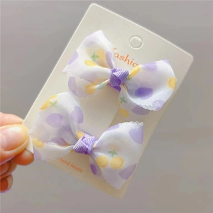 Détail de nœuds à cheveux avec pois violets et cerises jaunes sur carte blanche